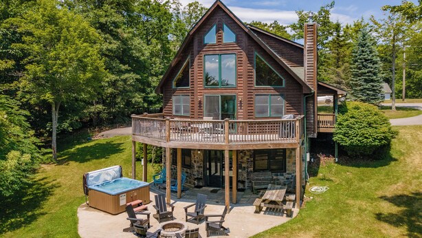 A two-story wooden cabin with a balcony, outdoor seating area, and a hot tub. - Scenic Retreat w/ Pool Table & Lake Views (Swanton)