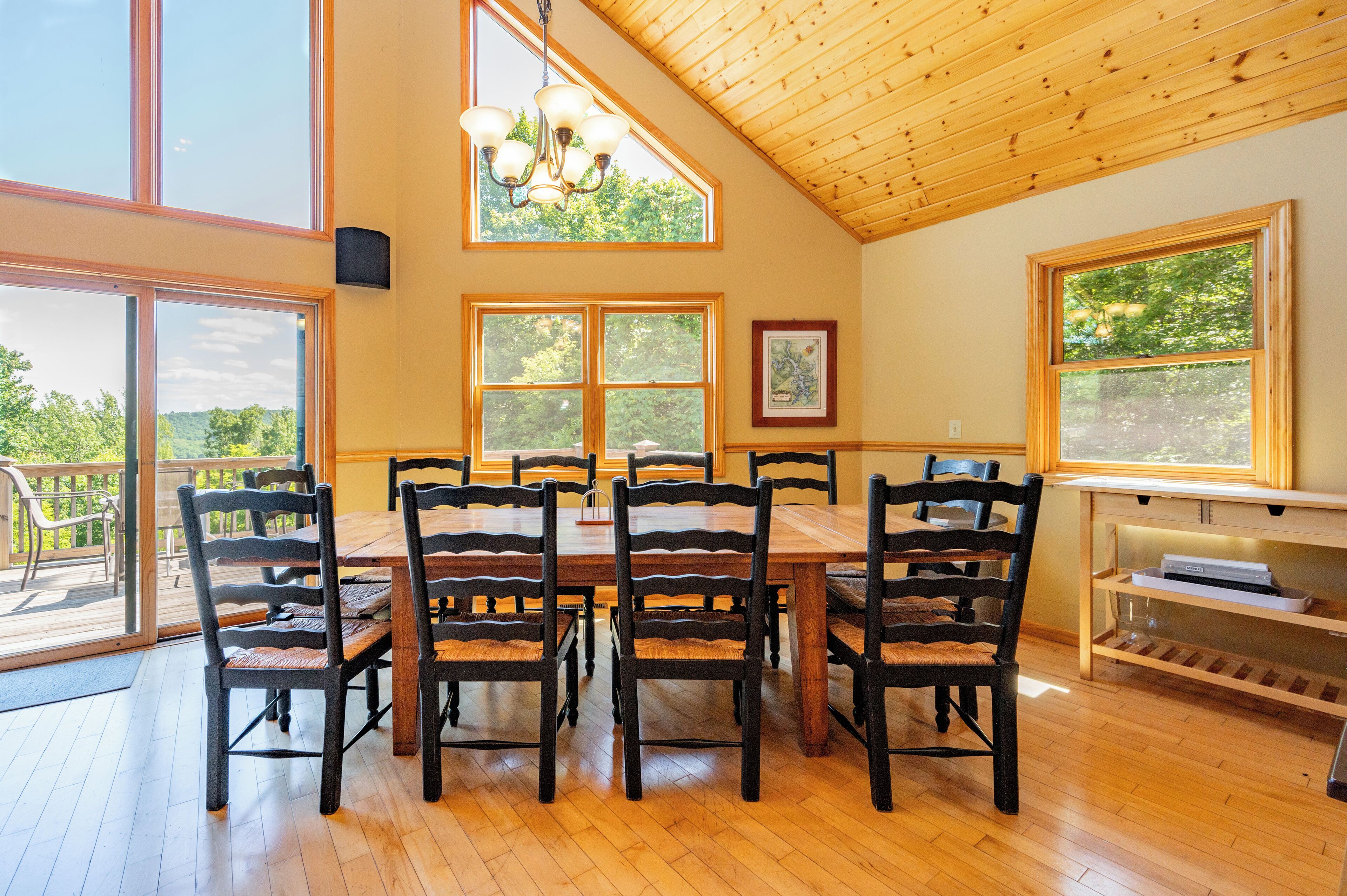 A dining area with a wooden table and chairs, large windows, and a ceiling with wooden beams.