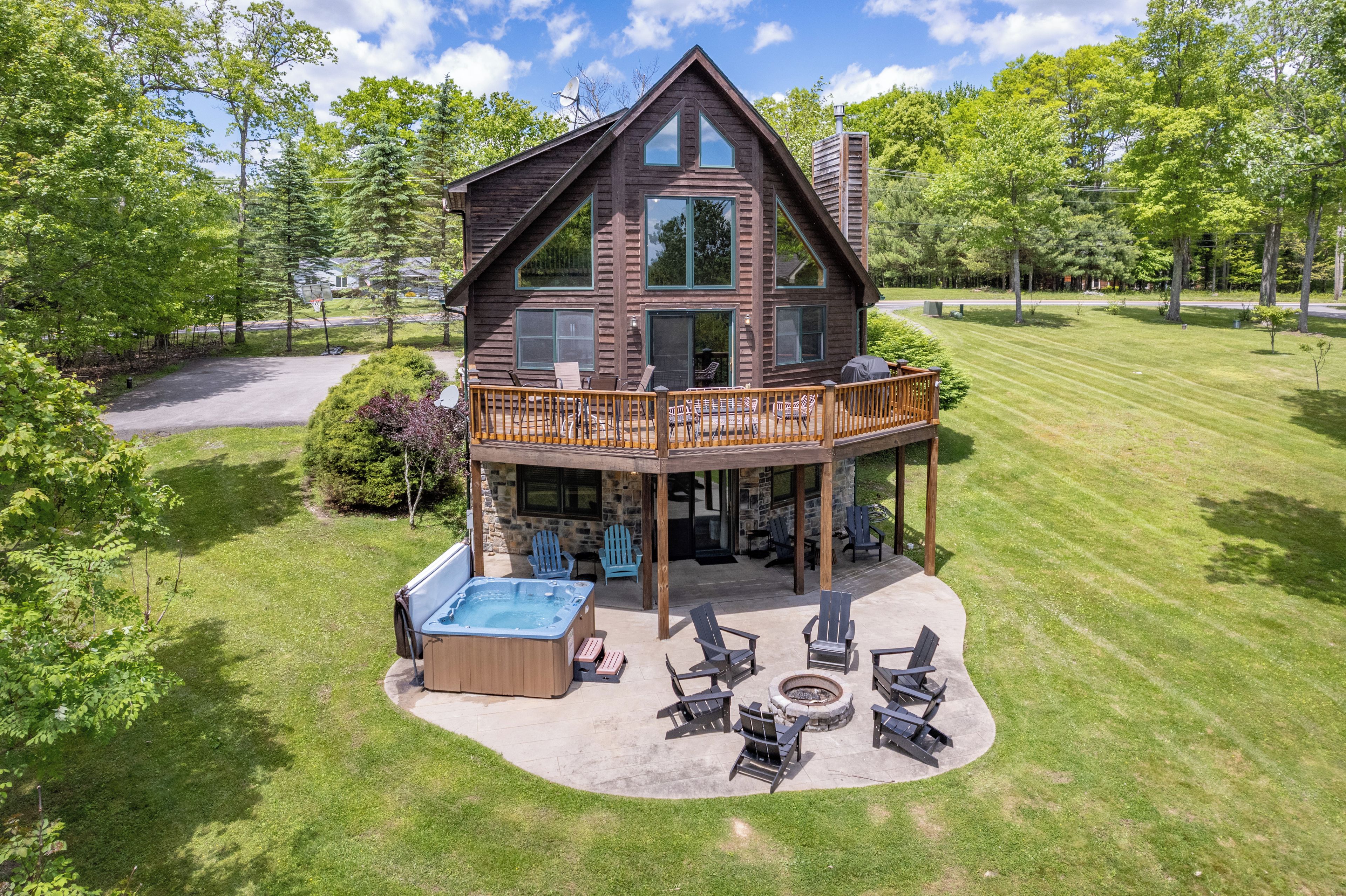 A two-story log cabin with a deck, outdoor seating, and a hot tub.