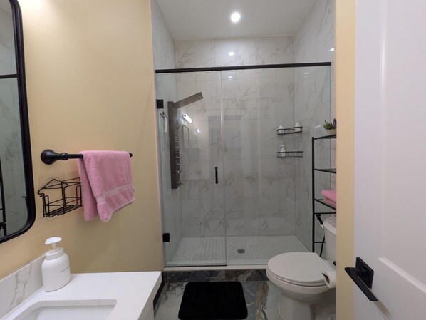 A modern bathroom with a glass-enclosed shower, a toilet, and a sink with a soap dispenser.