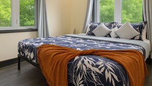 Ein Schlafzimmer mit einem Bett, zwei Fenstern und Blick auf Bäume.
