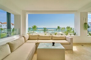 Una sala moderna con un ventanal grande que da a una playa y palmeras.