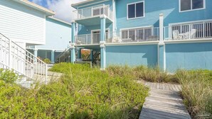 A two-story building with a light blue exterior, white railings, and a wooden deck leading to the entrance. - Portside Villas Unit 6 (Pensacola Beach)