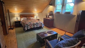 A cozy attic bedroom with a wooden ceiling, a bed with a patterned bedspread, a small table, a chair, and a dresser. - 2-bedroom cabin nestled in the Adirondack Park (Northville)