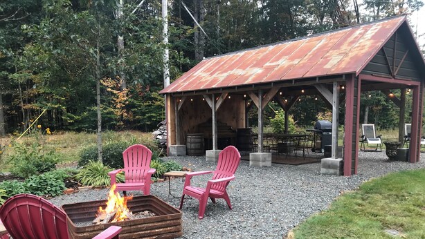 A rustic outdoor seating area with Adirondack chairs, a fire pit, and a covered pavilion with string lights. - 2-bedroom cabin nestled in the Adirondack Park (Northville)
