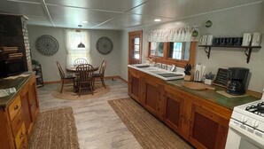 A kitchen with wooden cabinets, a central island, a dining table with chairs, and a built-in oven. - 2-bedroom cabin nestled in the Adirondack Park (Northville)