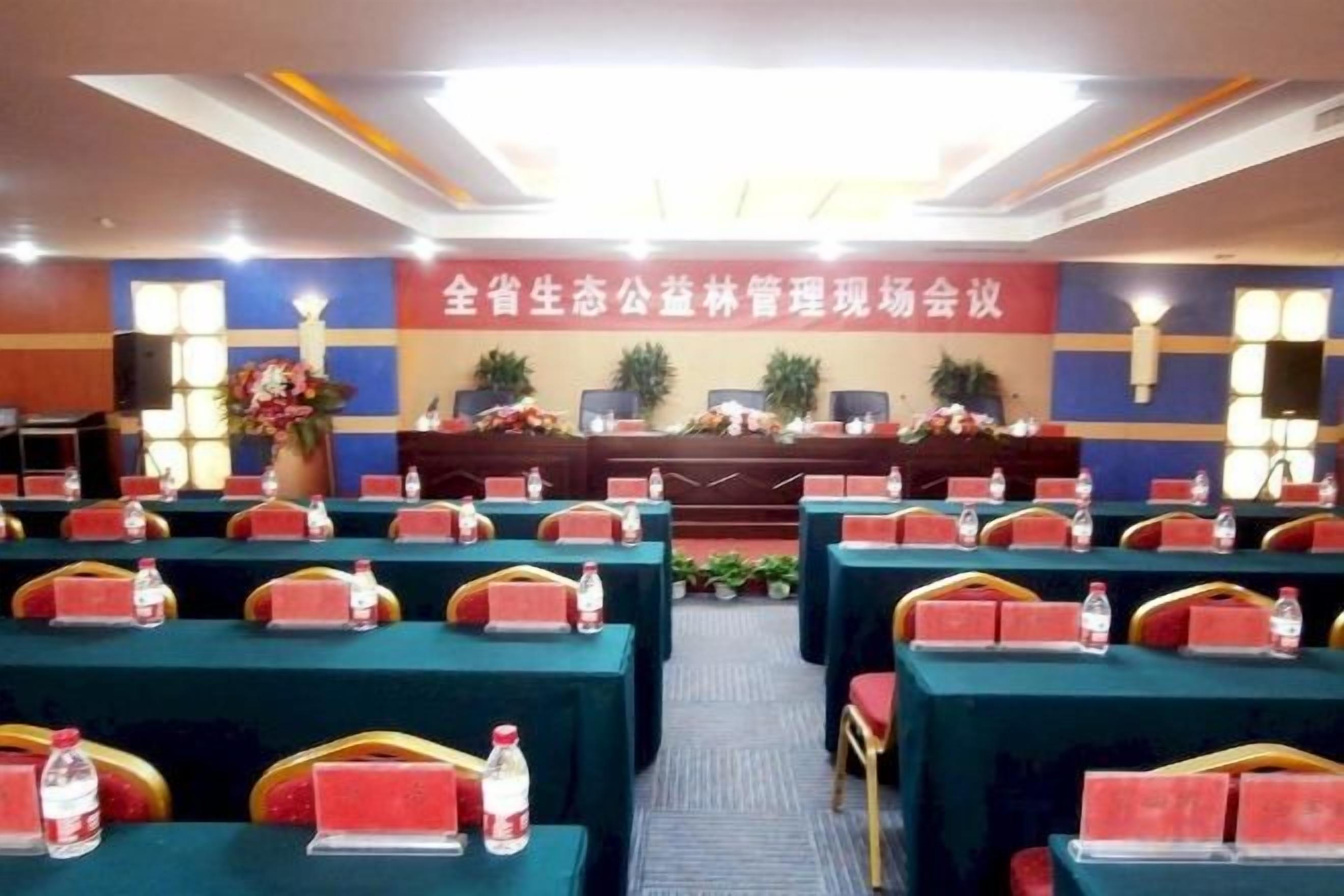 A conference room with rows of tables and chairs, a stage with a podium, and a banner with text.