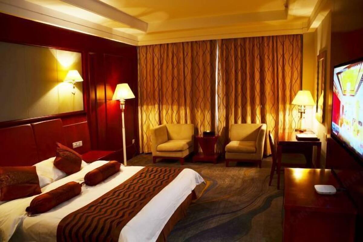 Une chambre d’hôtel avec un lit, deux fauteuils, une télévision et un bureau.