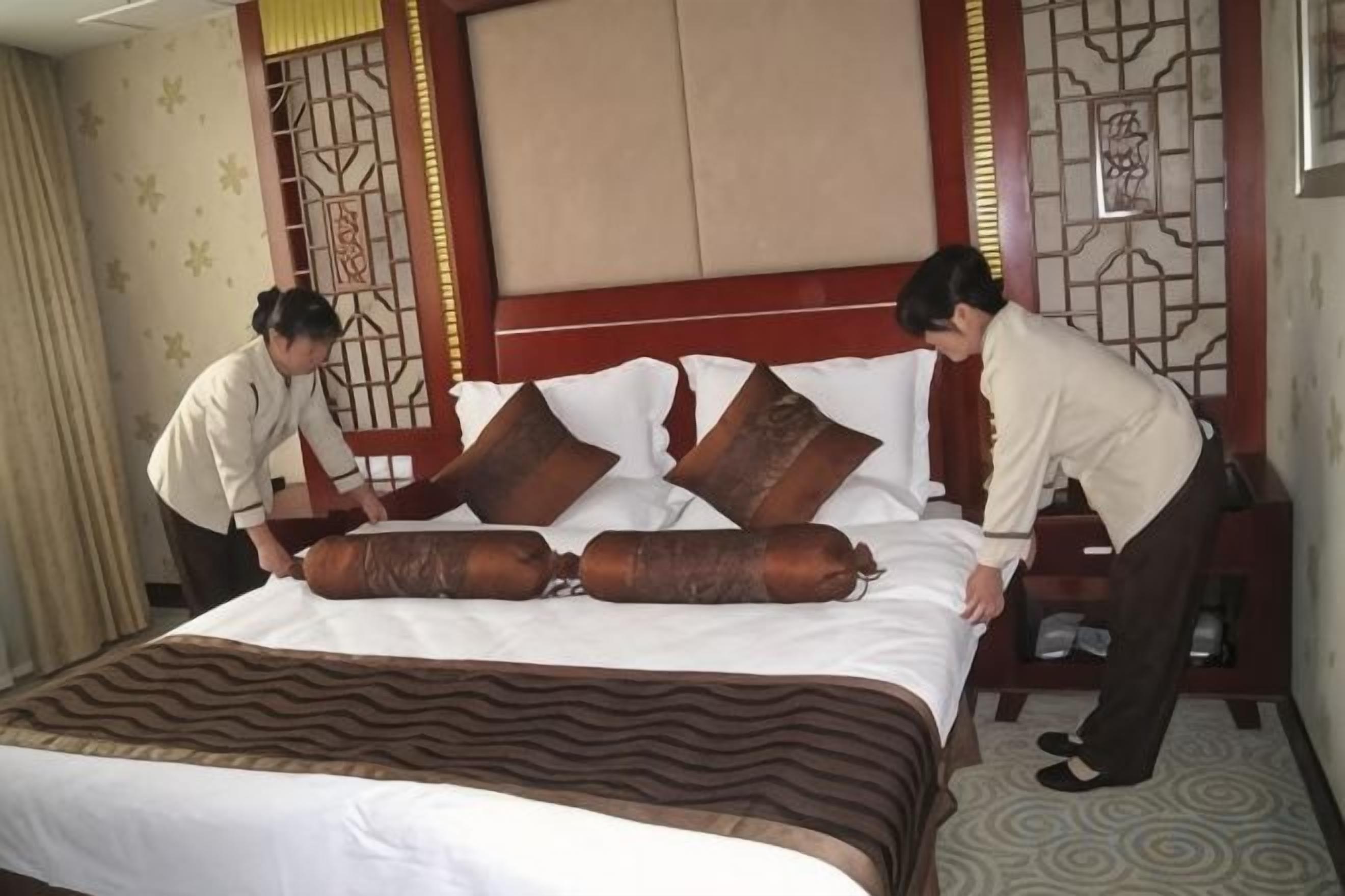 A hotel room with a large bed, a headboard with a decorative panel, and a nightstand with a lamp.