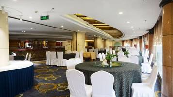 A banquet hall with round tables, white chairs, and a carpeted floor.