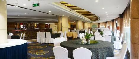 Un salón de banquetes con mesas redondas, sillas blancas y piso alfombrado.