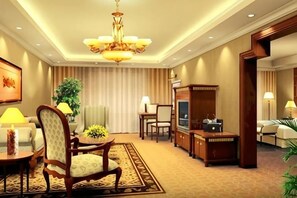 Een hotelkamer met een kroonluchter, een eettafel met stoelen, een televisie en een bank.