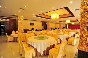 Un salón de banquetes con mesas redondas, sillas amarillas y una araña de cristal.