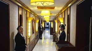 A hotel corridor with a polished floor, wall-mounted lamps, and a reception desk. - Yunshuijian Hotel (Jiaozuo)