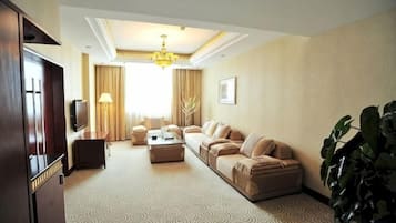 Un salón de hotel con un conjunto de sofás, una mesa de centro, un televisor y una planta grande.