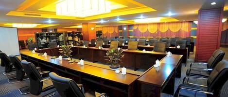 A conference room with multiple tables and chairs, equipped with a projector screen and a whiteboard.
