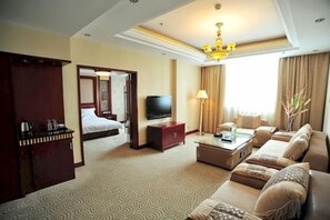 Une chambre d’hôtel comprenant un lit, une télévision, un canapé, une table basse et un bureau avec une lampe.
