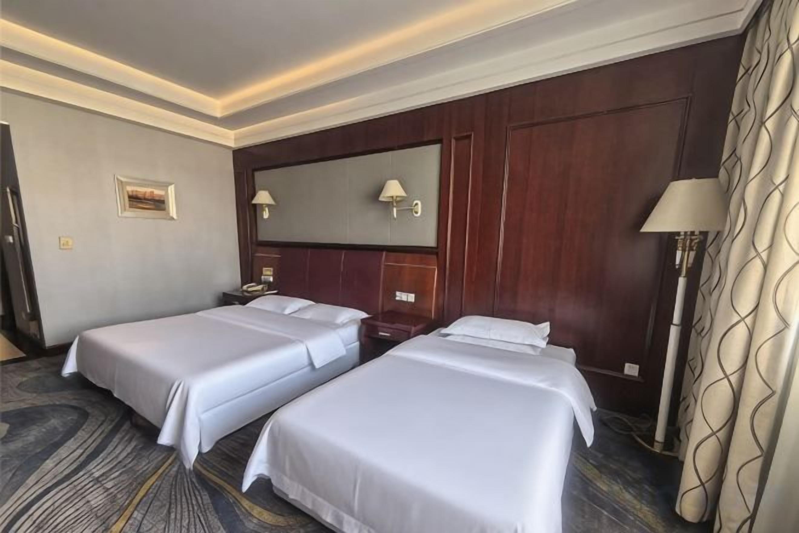 A hotel room with two beds, a large mirror, a nightstand, and a lamp.