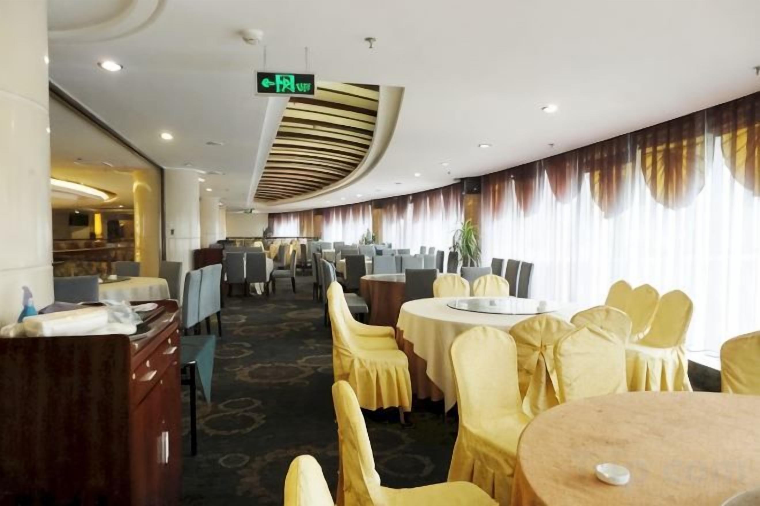 A hotel dining area with round tables, yellow chairs, and a view of the bar area.