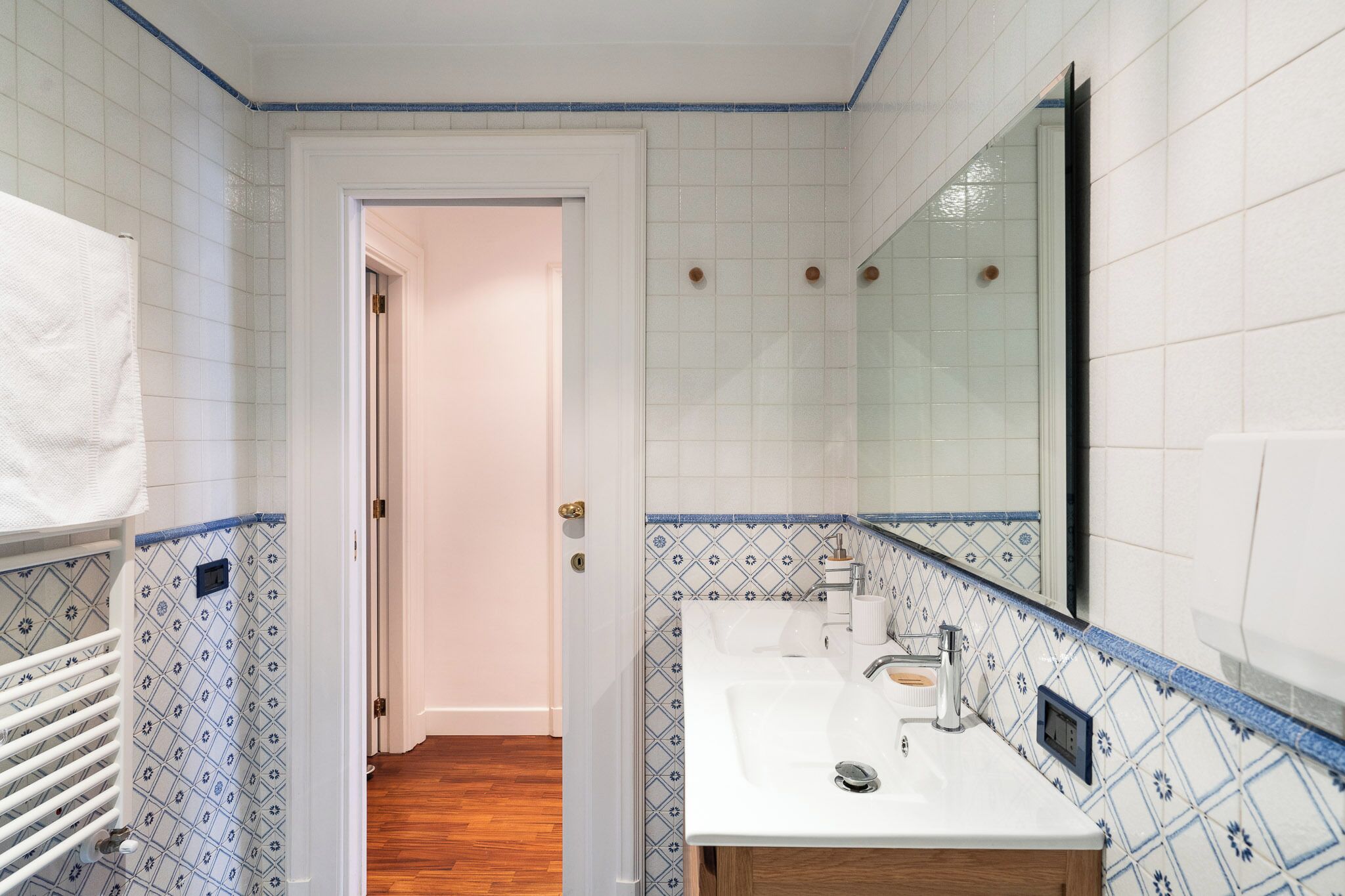 Un baño con lavamanos blanco, espejo y azulejos estampados.