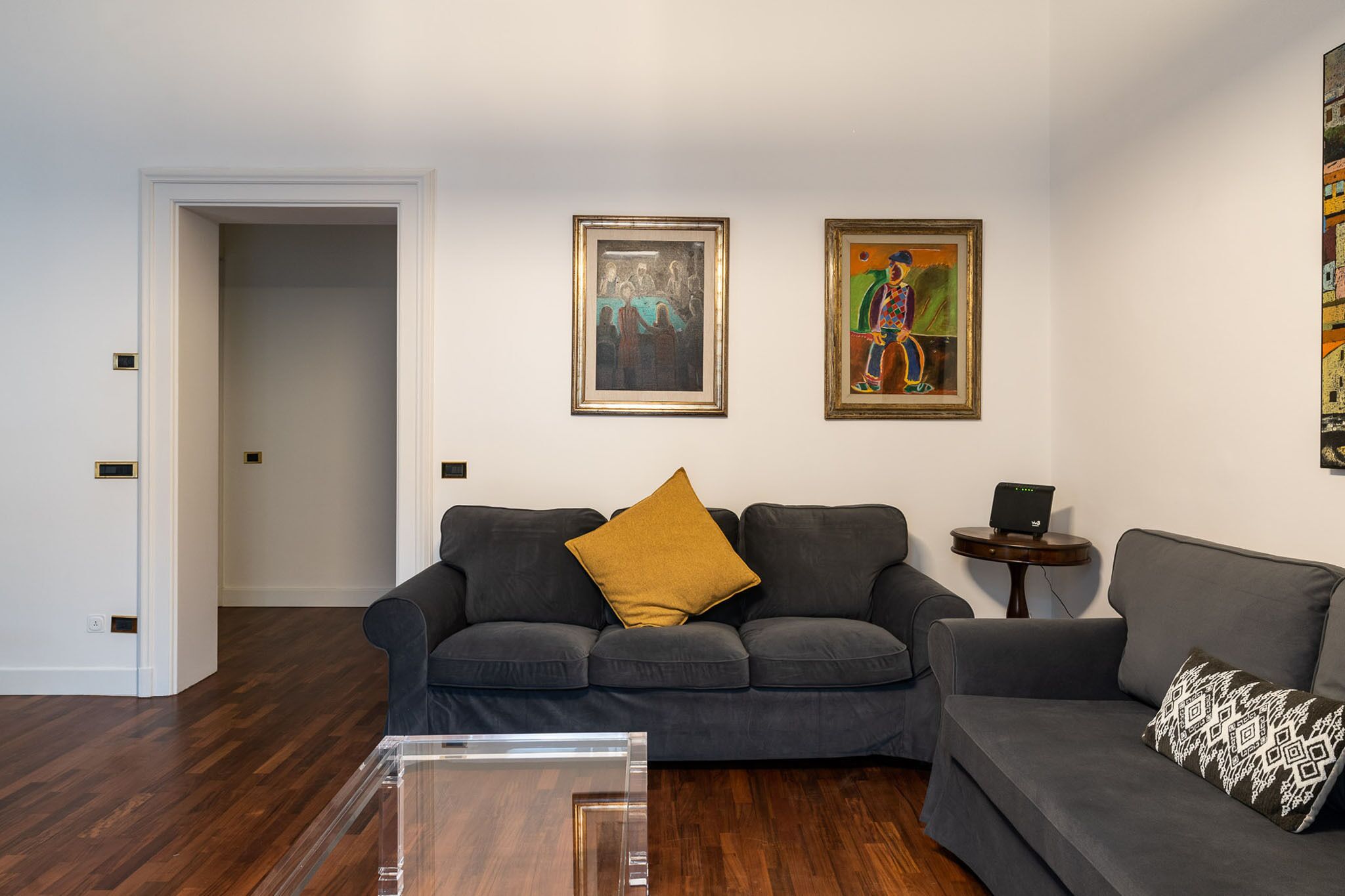 A living room with a grey sofa, a coffee table, and two paintings on the wall.