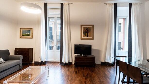 Ein modernes Wohnzimmer mit einer Couch, einem Glastisch, einem Fernseher auf einem Holzboden und einem Essbereich mit Stühlen.