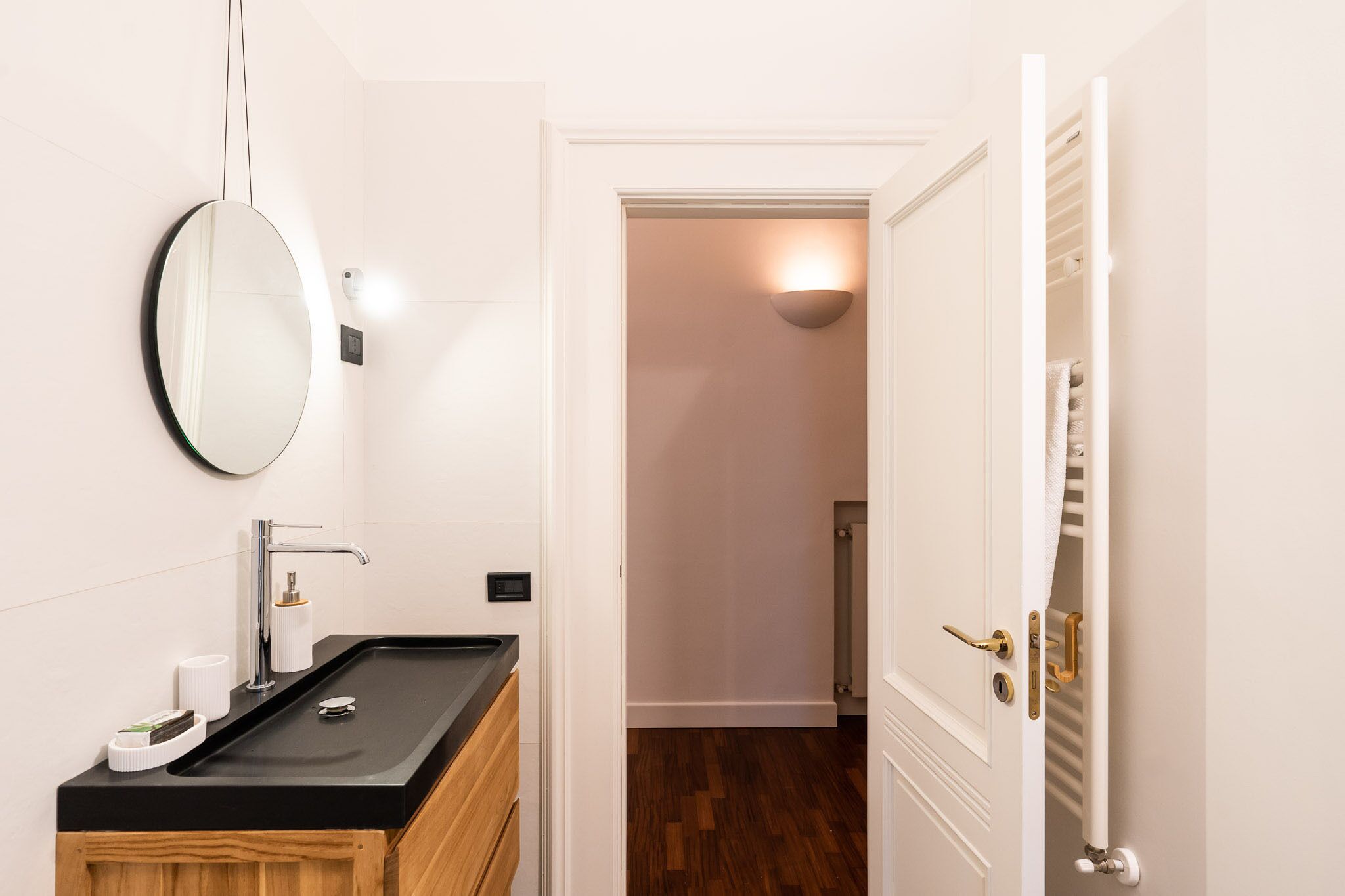A modern bathroom with a black sink, a round mirror, and a white door leading to a hallway.