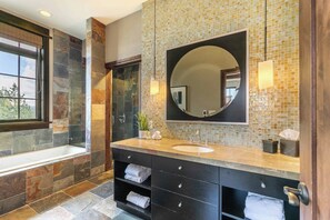 Une salle de bain avec un mur en pierre, un grand miroir, un lavabo et une fenêtre.