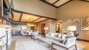 A spacious living room with a fireplace, a sofa, armchairs, and a coffee table. There is a kitchen in the background with modern appliances.