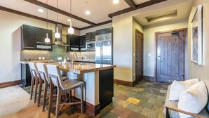 A modern kitchen with dark cabinets, a central island with bar stools, stainless steel appliances, and pendant lighting.