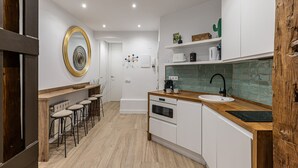 A modern kitchen with white cabinets, a wooden countertop, and a backsplash. There are stools at the bar area, and a large mirror on the wall.