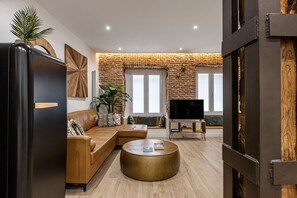 A modern living room with a leather sofa, a round coffee table, and a flat-screen TV. - Waou Las Letras VI - Alquiler Corta Duración (Madrid)