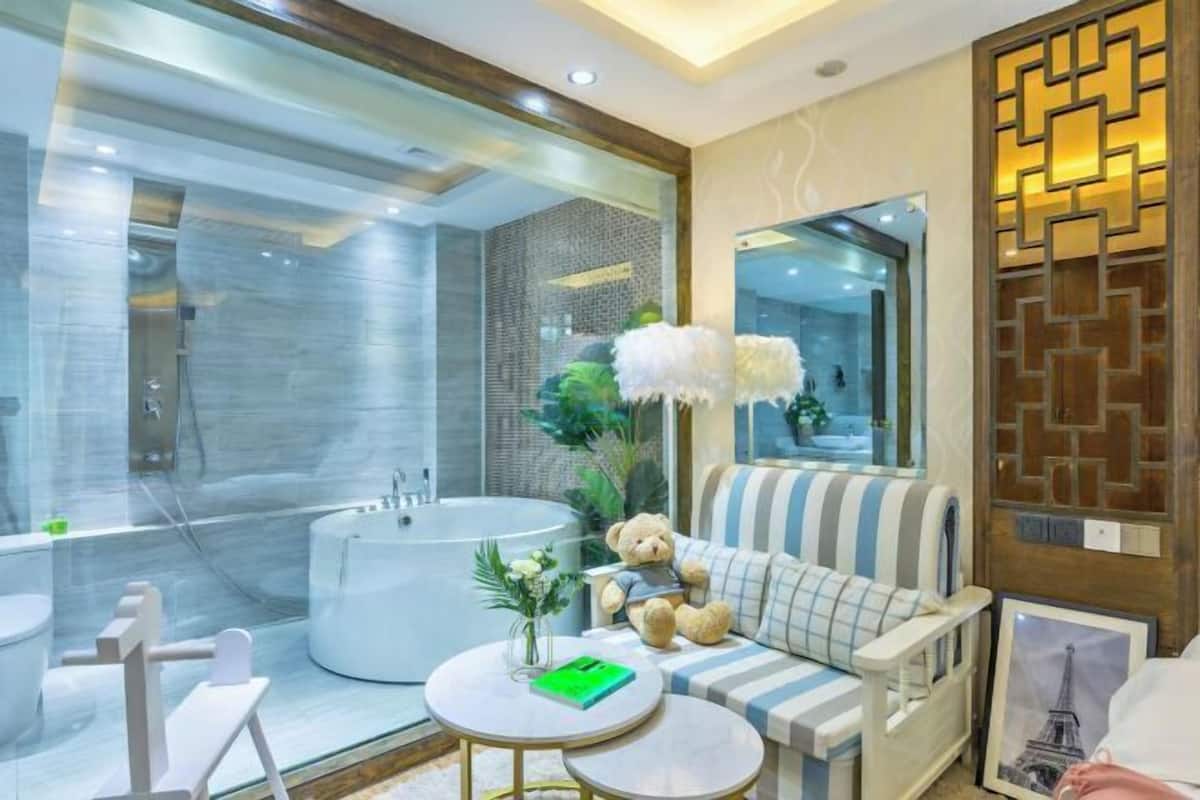 A modern bathroom with a large bathtub, a sofa with a striped cushion, a teddy bear, and a small round table with a green book.