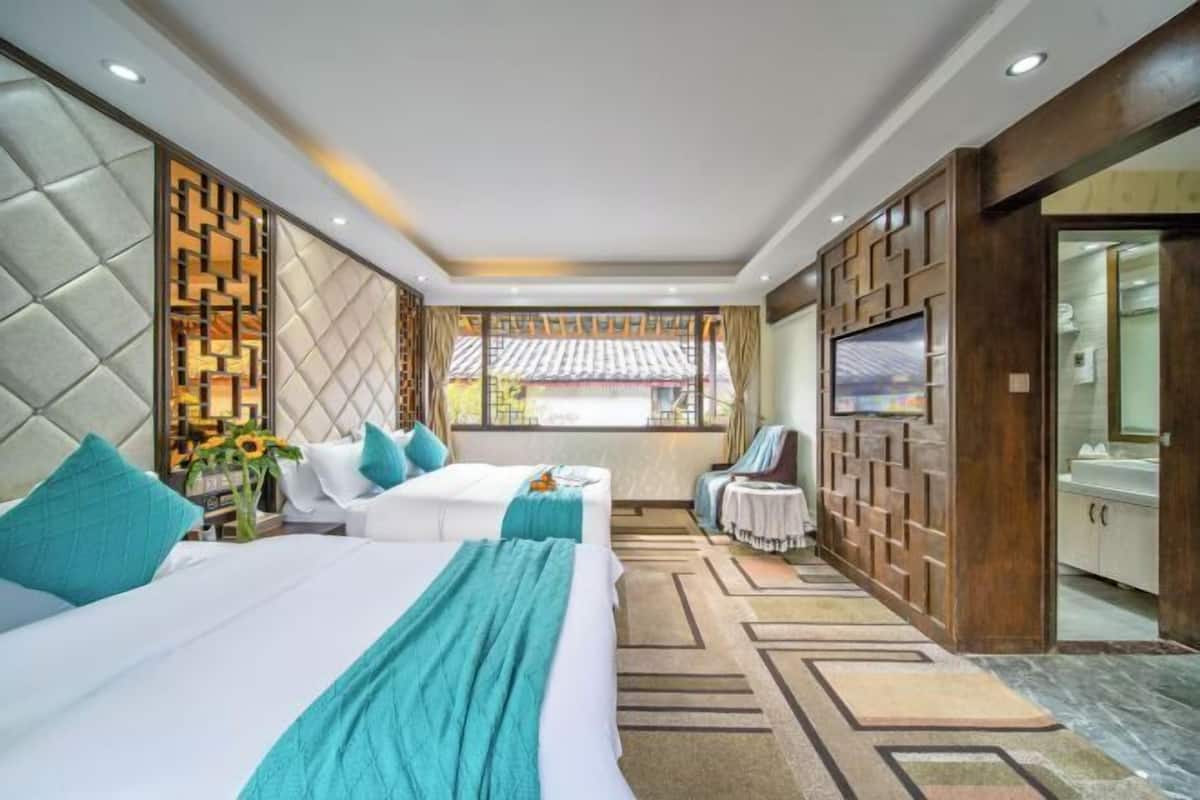 A hotel room with two beds, a TV, a small table, and a view of the outside.