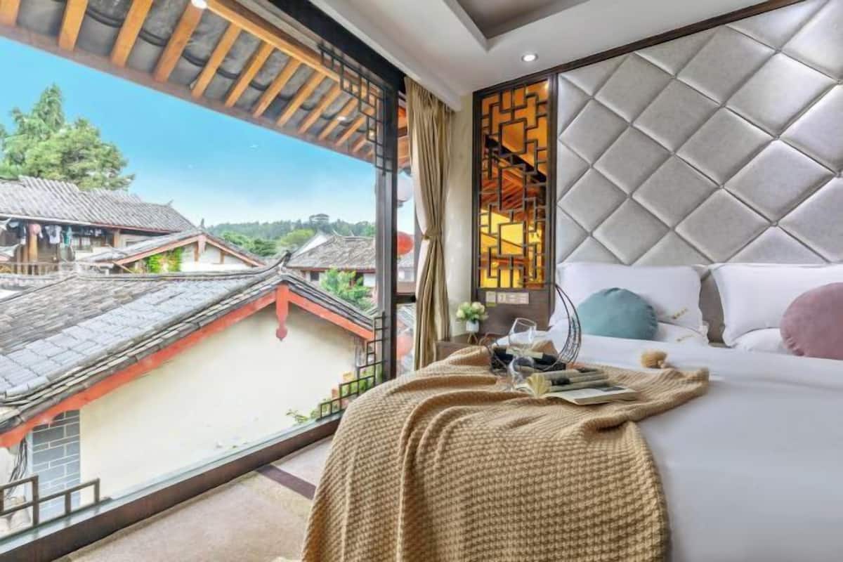 A hotel room with a large window, a bed with a decorative headboard, and a view of traditional buildings.