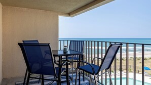Varanda com mesa e cadeiras, vista para uma praia e uma piscina.