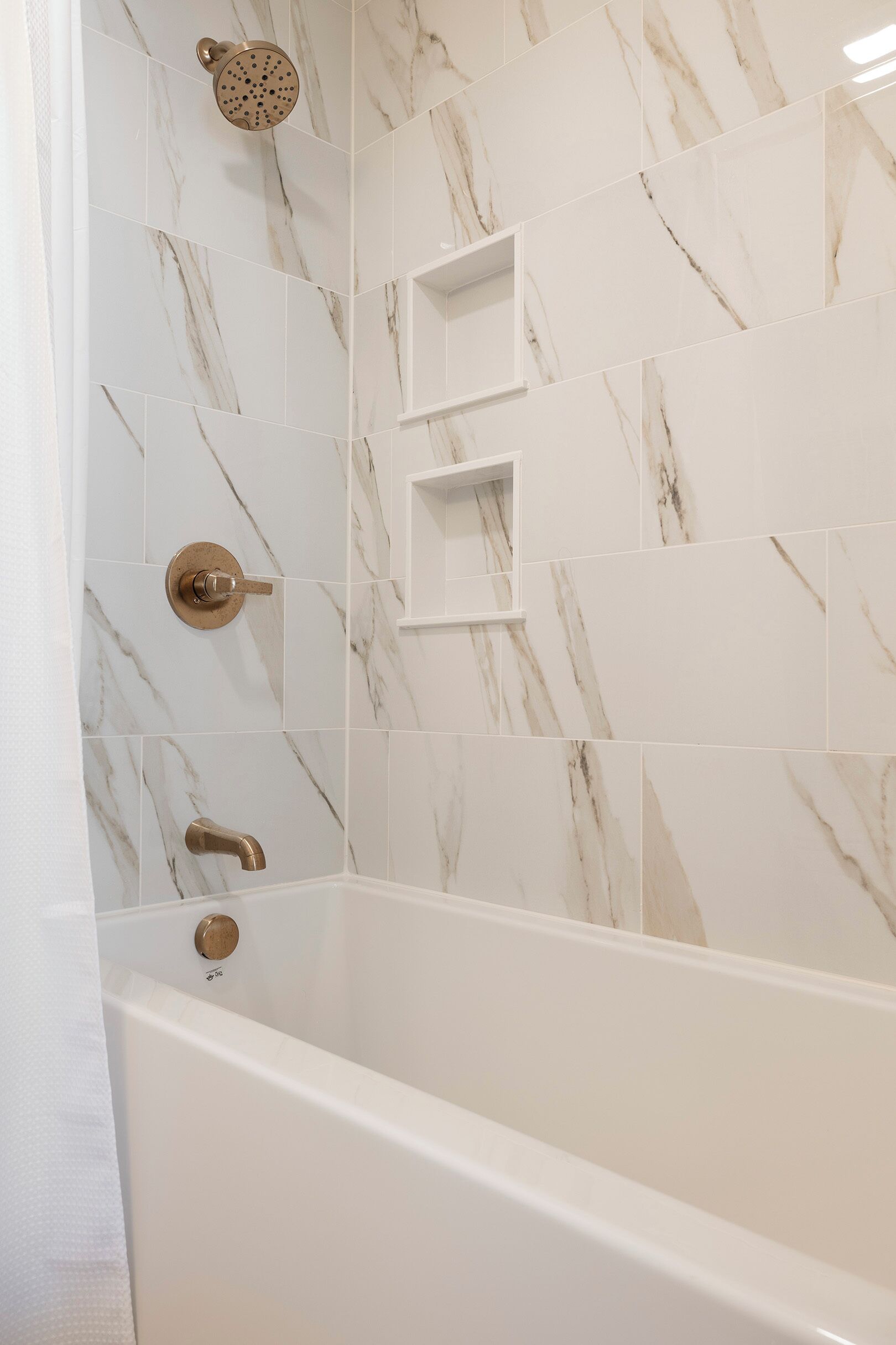 A bathroom with a bathtub, a showerhead, and marble-patterned tiles.