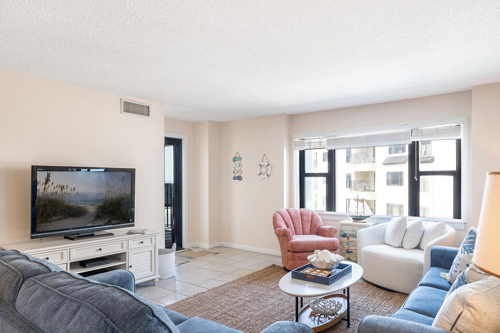 A living room with a television, a sofa, a chair, and a window with a view of buildings.