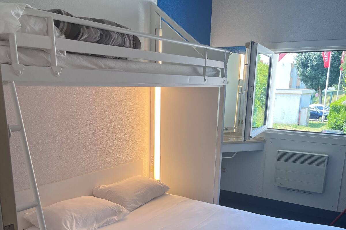 Una cama litera con ropa blanca y una ventana que da a vistas del exterior.