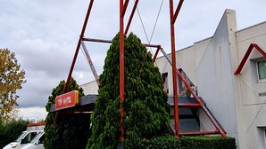 Un letrero de hotel con una combinación de colores rojo y azul, un marco metálico rojo y un gran árbol al frente.
