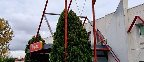 A hotel sign with a red and blue color scheme, a red metal frame, and a large tree in front.