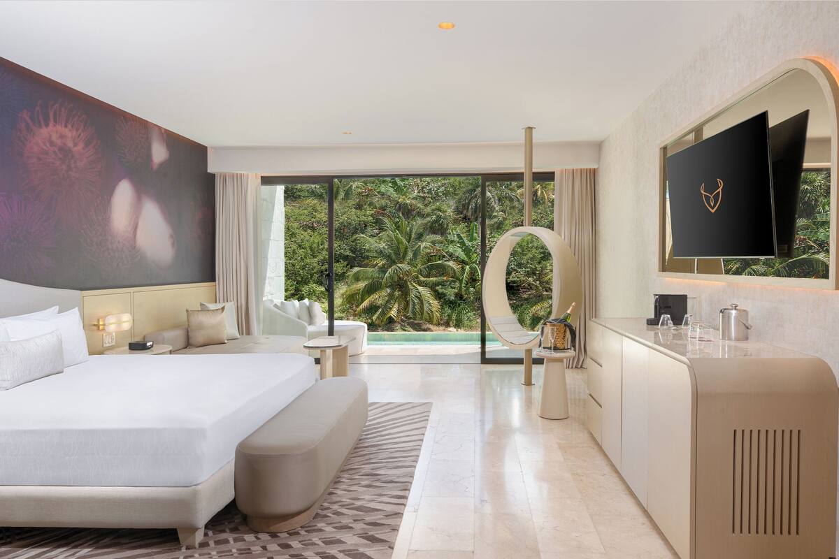 Quarto de hotel moderno com uma cama grande, área de estar, televisão e vista para o exterior.