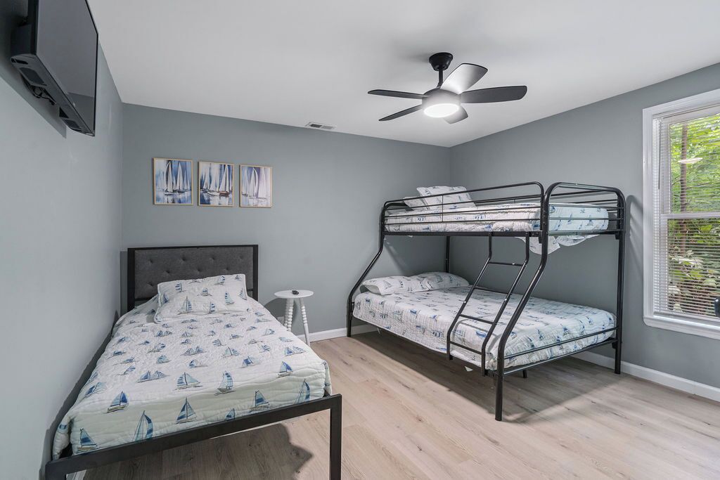 A bedroom with a single bed, a bunk bed, a ceiling fan, and a window with blinds.