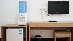 A small kitchenette with a water dispenser, a refrigerator, a trash can, and a television on a wooden desk. - Fu Gang Hotel (Guangzhou)