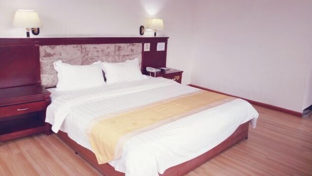 A neatly made bed with a wooden headboard, a bedside table with a lamp, and a nightstand with a phone. - Fu Gang Hotel (Guangzhou)