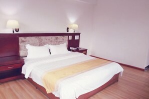 A neatly made bed with a wooden headboard, a bedside table with a lamp, and a nightstand with a phone. - Fu Gang Hotel (Guangzhou)