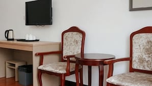 A room with a desk, two chairs, a television, a coffee maker, and a trash bin. - Fu Gang Hotel (Guangzhou)