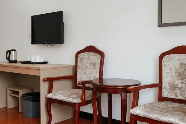 A room with a desk, two chairs, a television, a coffee maker, and a trash bin. - Fu Gang Hotel (Guangzhou)
