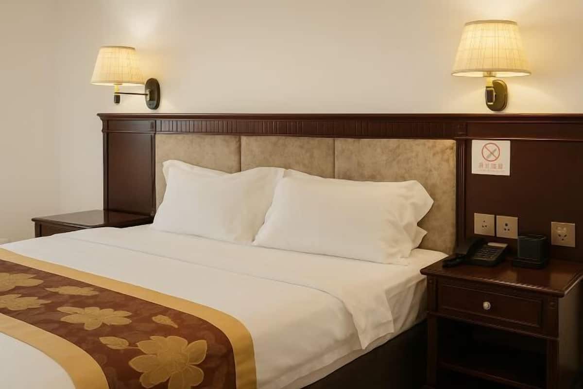 Una habitación de hotel con una cama, dos lámparas de noche, una mesita de noche con un teléfono y un cartel que indica que no se permite fumar.