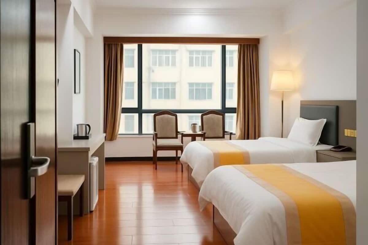 Habitación de hotel con dos camas, un escritorio, una silla, una ventana con cortinas y una lámpara.